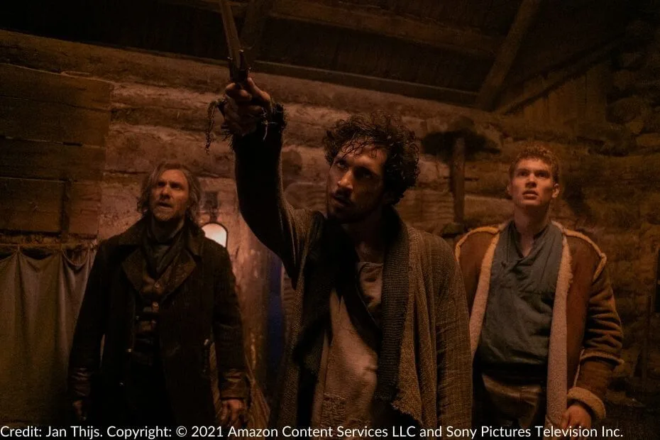 Mat raises the ruby-hilted dagger from Shadar Logoth in the Grinwell farmhouse, his intense expression fixed on something unseen. Thom and Rand stand behind him, watching in confusion and concern.