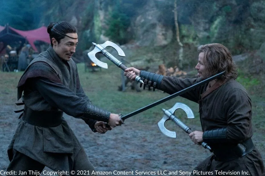 Lan and Stepin spar at the Aes Sedai camp. Lan wields his sword precisely, while Stepin counters with a dual-bladed axe.