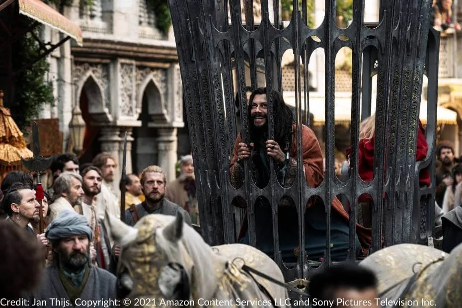 Logain grins menacingly through the bars of his cage as it is paraded through the bustling streets of Tar Valon, surrounded by onlookers and guards.