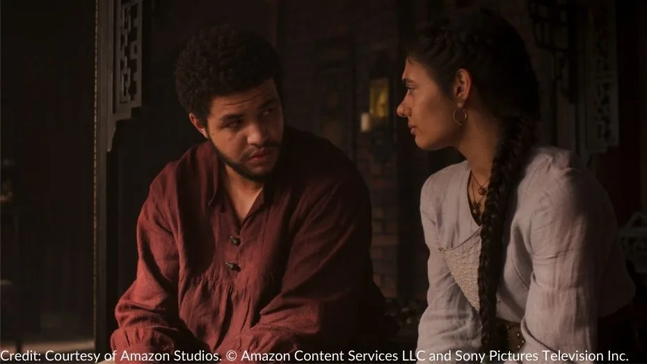 Perrin and Egwene sit together, engaged in a heartfelt conversation, with soft lighting illuminating their expressions.