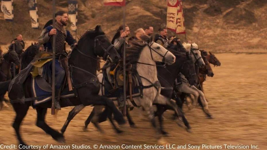 A Shienaran cavalry unit, led by warriors in armor, gallops across a field under banners with sigils, heading towards Tarwin's Gap.