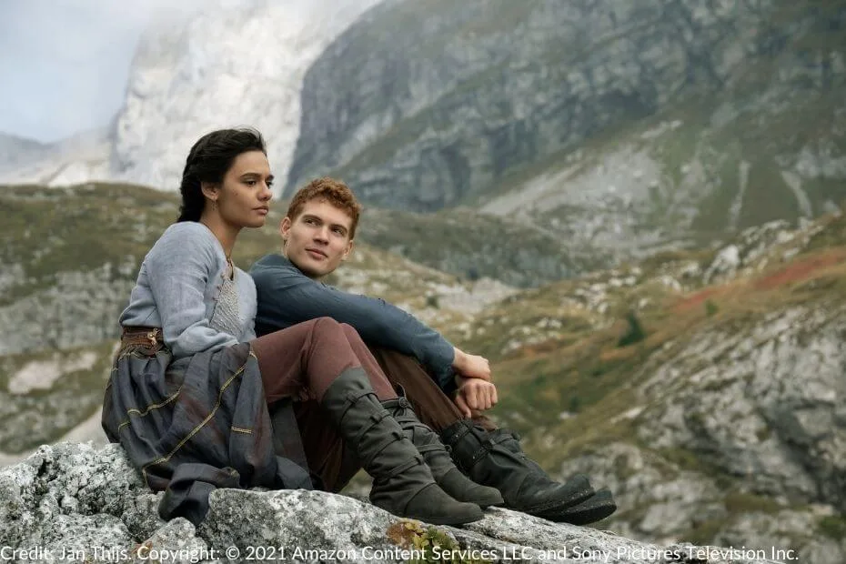 Rand and Egwene sit together on a rocky outcrop in a mountainous landscape, reflecting the pastoral beauty of the Two Rivers in The Wheel of Time.